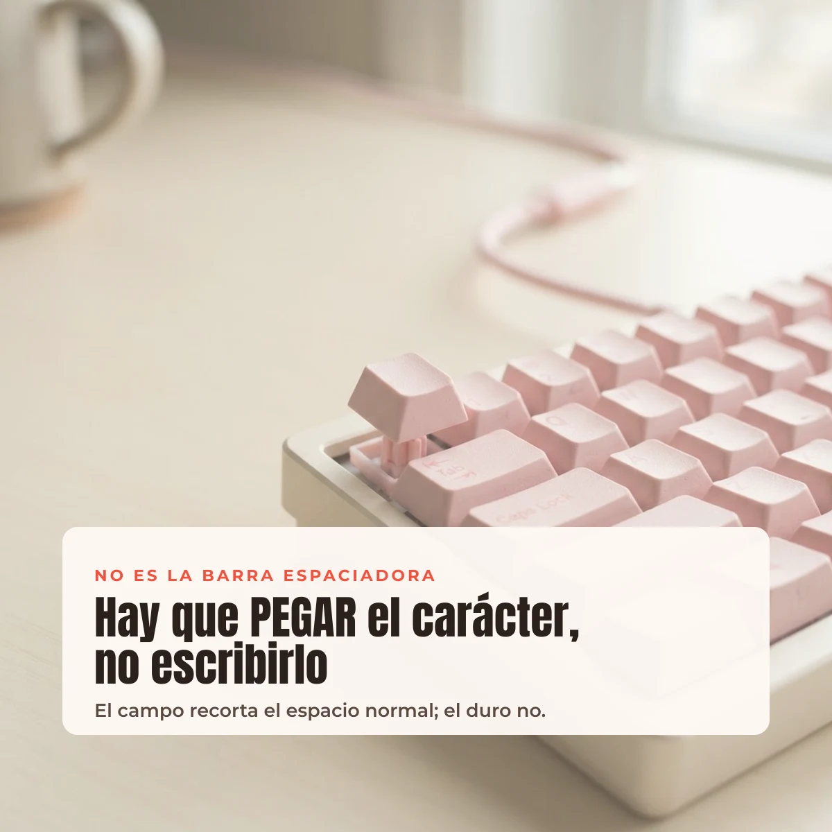 Teclado mecánico rosa sobre escritorio crema con el aviso de que el espacio hay que pegarlo, no escribirlo